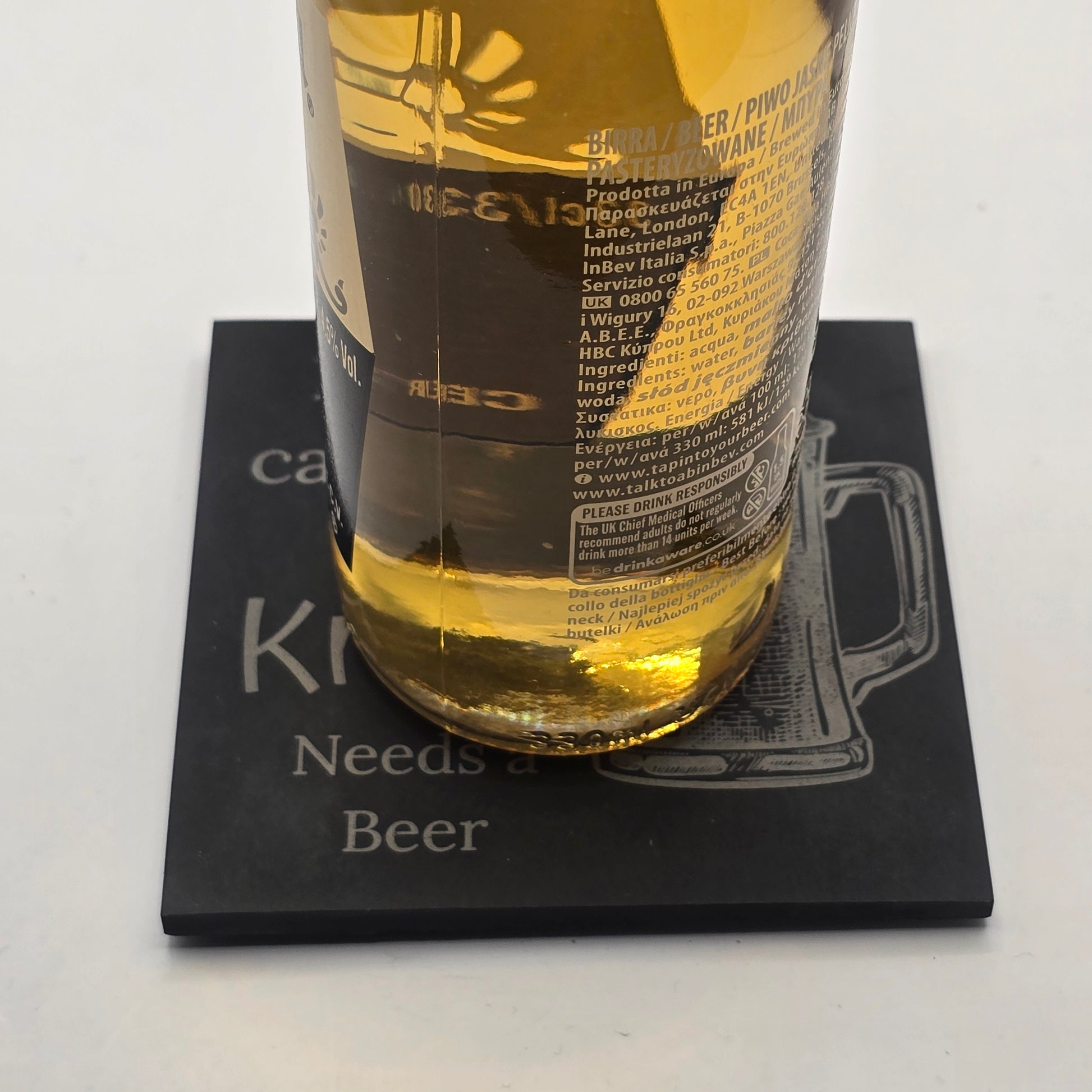 Bottle of beer resting on a black slate coaster with  a 'Beer' quote on a white background