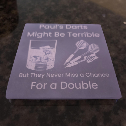 Custom slate coaster with humorous dart-themed text on a dark surface