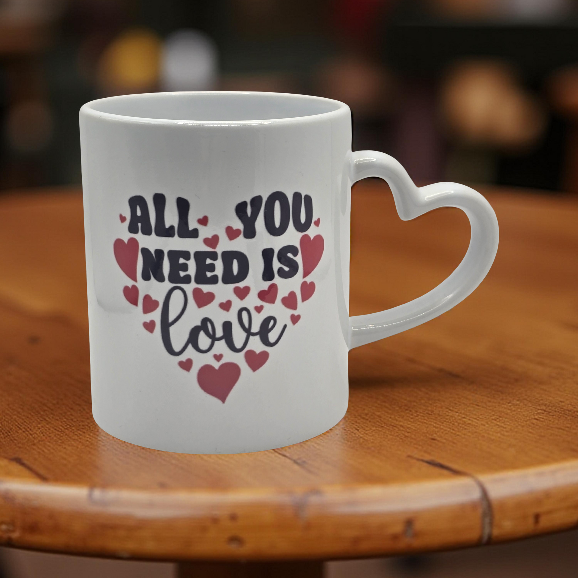 White mug with 'All You Need Is Love' text on a wooden table