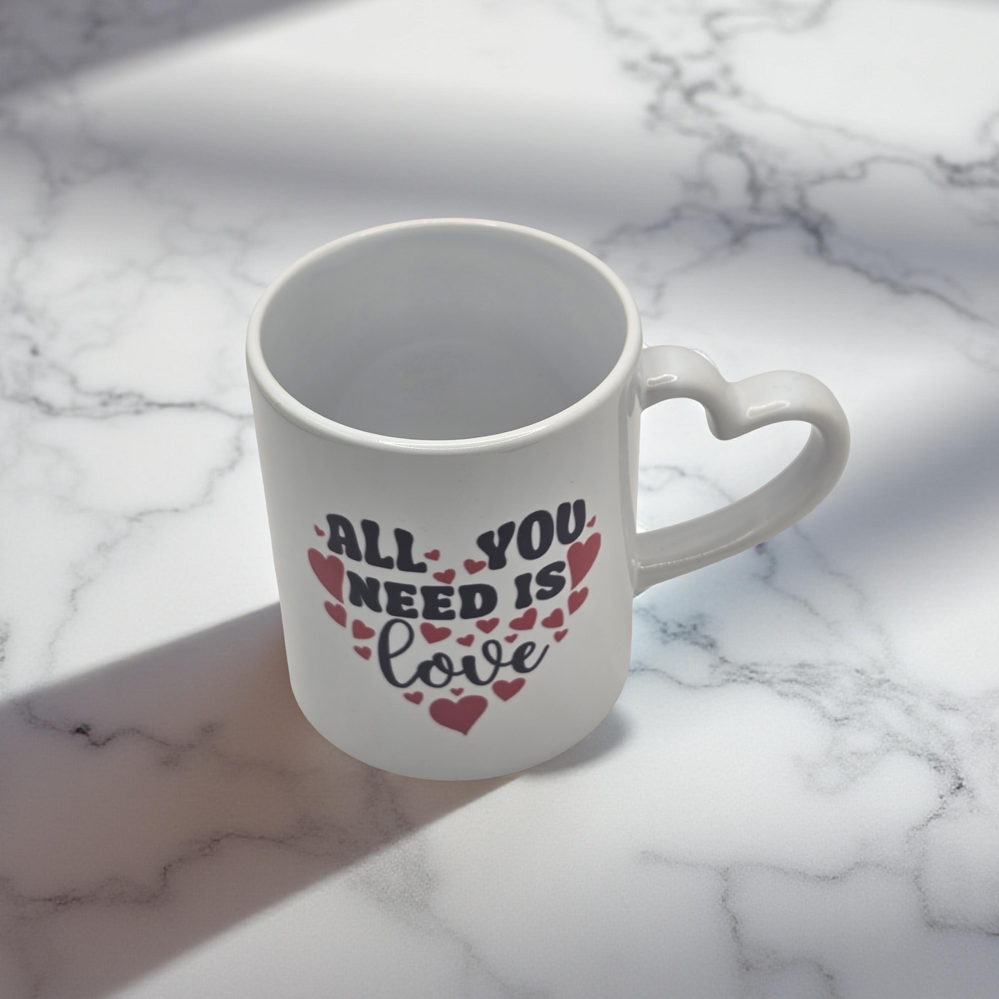 White mug with 'All You Need Is Love' text on a marble surface