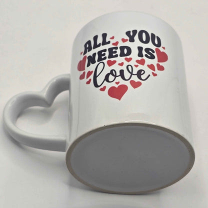 White mug with 'All You Need Is Love' text and heart designs on a white background showing the underside of the mug