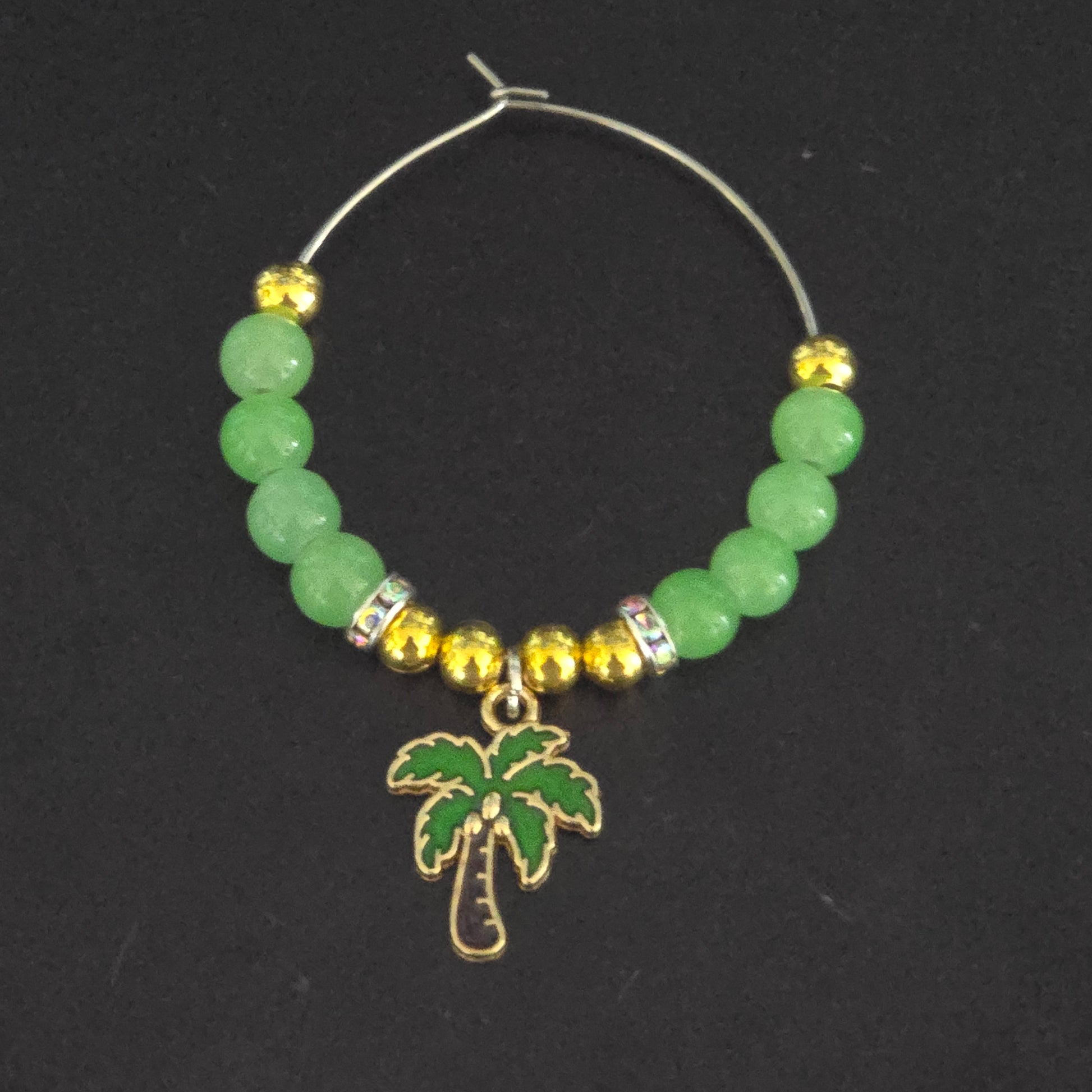 Beaded glass charm with green beads, gold accents, and a palm tree charm on a black background