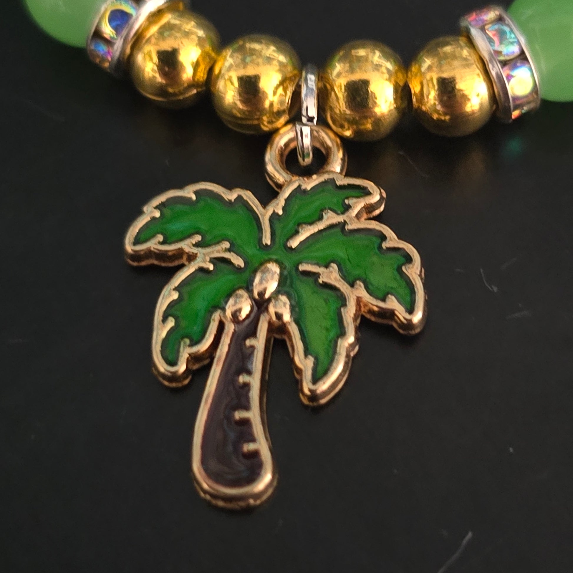 Close-up of a green and gold palm tree charm on a black background