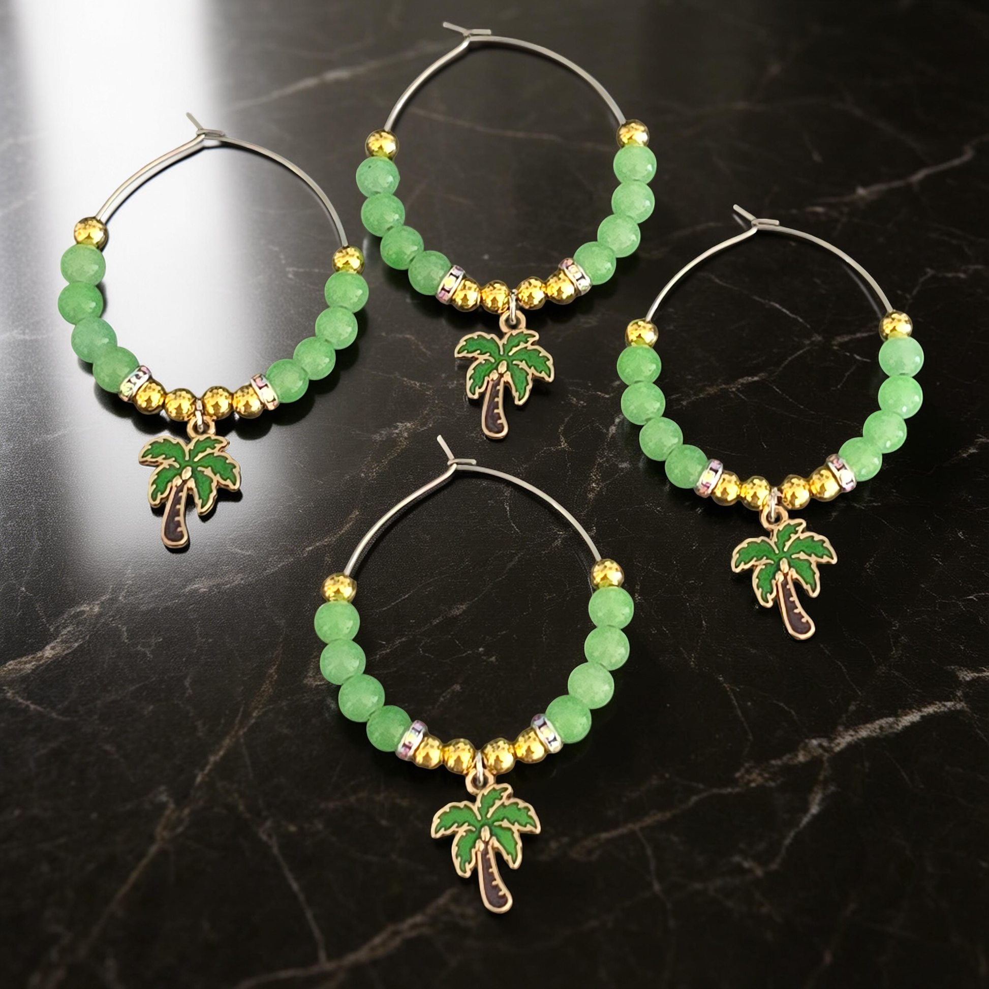 4 tropical wine glass charms with green beads and palm tree charms on a dark marble surface.