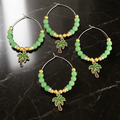 4 tropical wine glass charms with green beads and palm tree charms on a dark marble surface.