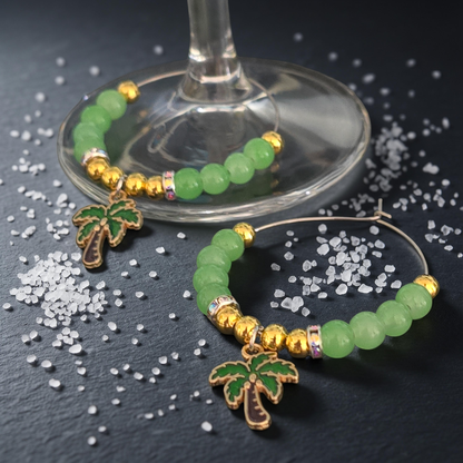 Green beaded Wine Glass charms with palm tree accent on a dark surface