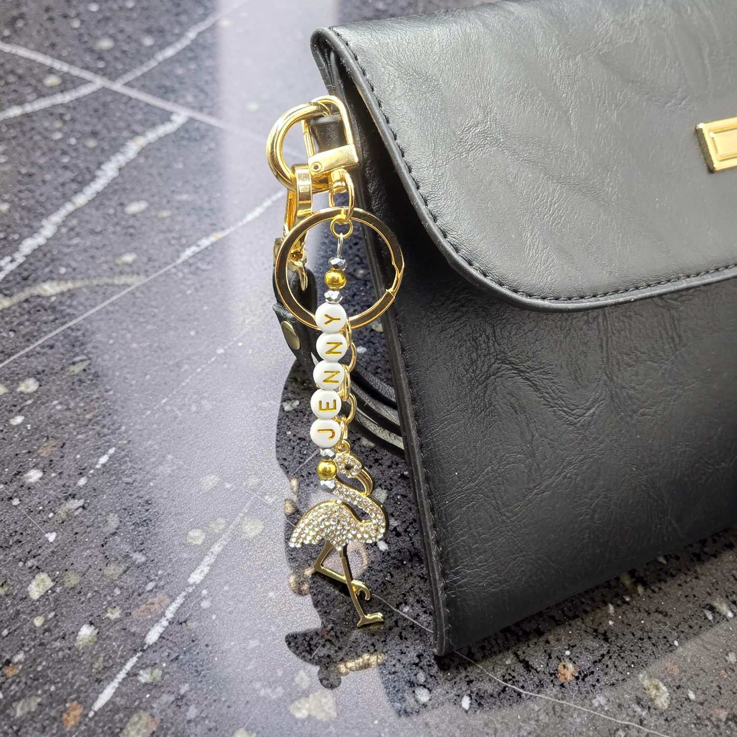 Gold and white flamingo keychain attached to a black handbag on a textured surface