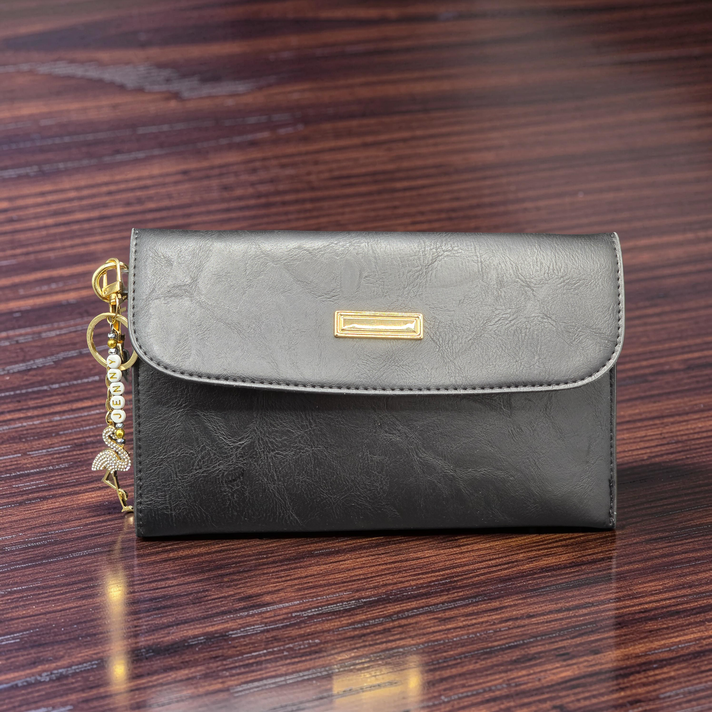 Black leather clutch bag with gold accent on a wooden surface with a rhinestone flamingo keychain.