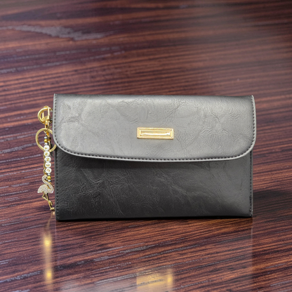 Black leather clutch bag with gold accent on a wooden surface with a rhinestone flamingo keychain.