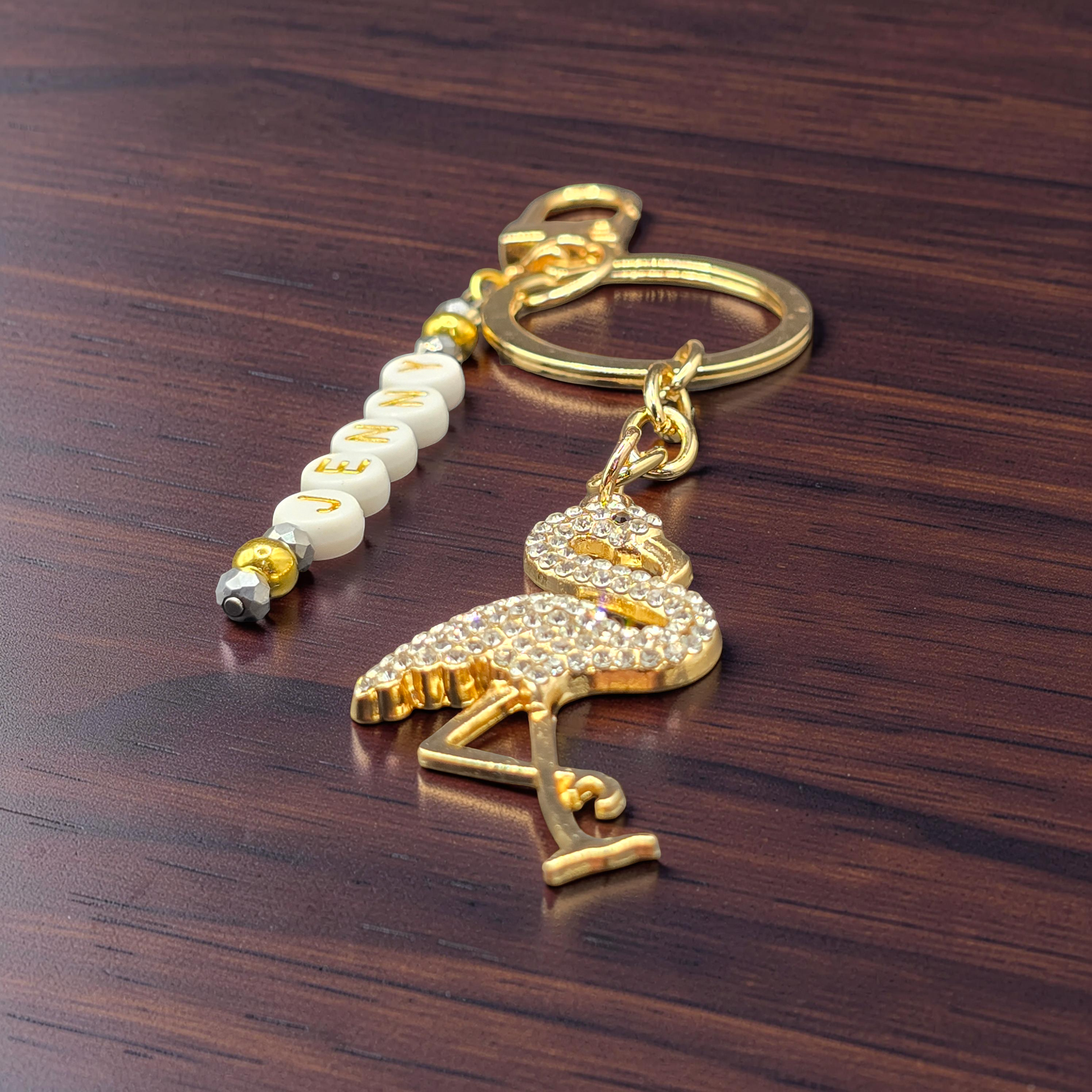 Gold flamingo keychain with lettered beads on a wooden surface