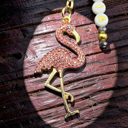 Pink flamingo keychain with gold accents and personalised letter beads highlighted in a spotlight