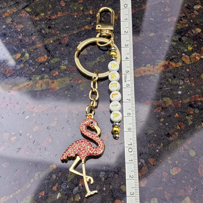 Flamingo keychain with 'AMELIA' beads next to a ruler on a textured surface