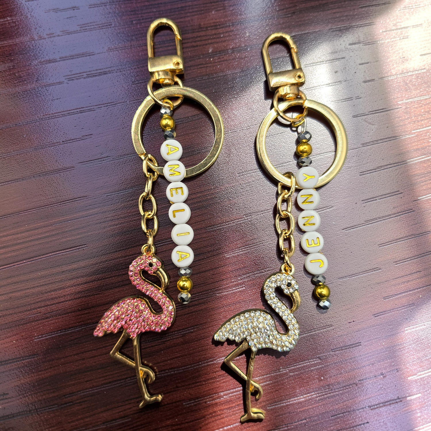 Two flamingo keychains with decorative personalised chains on a wooden surface