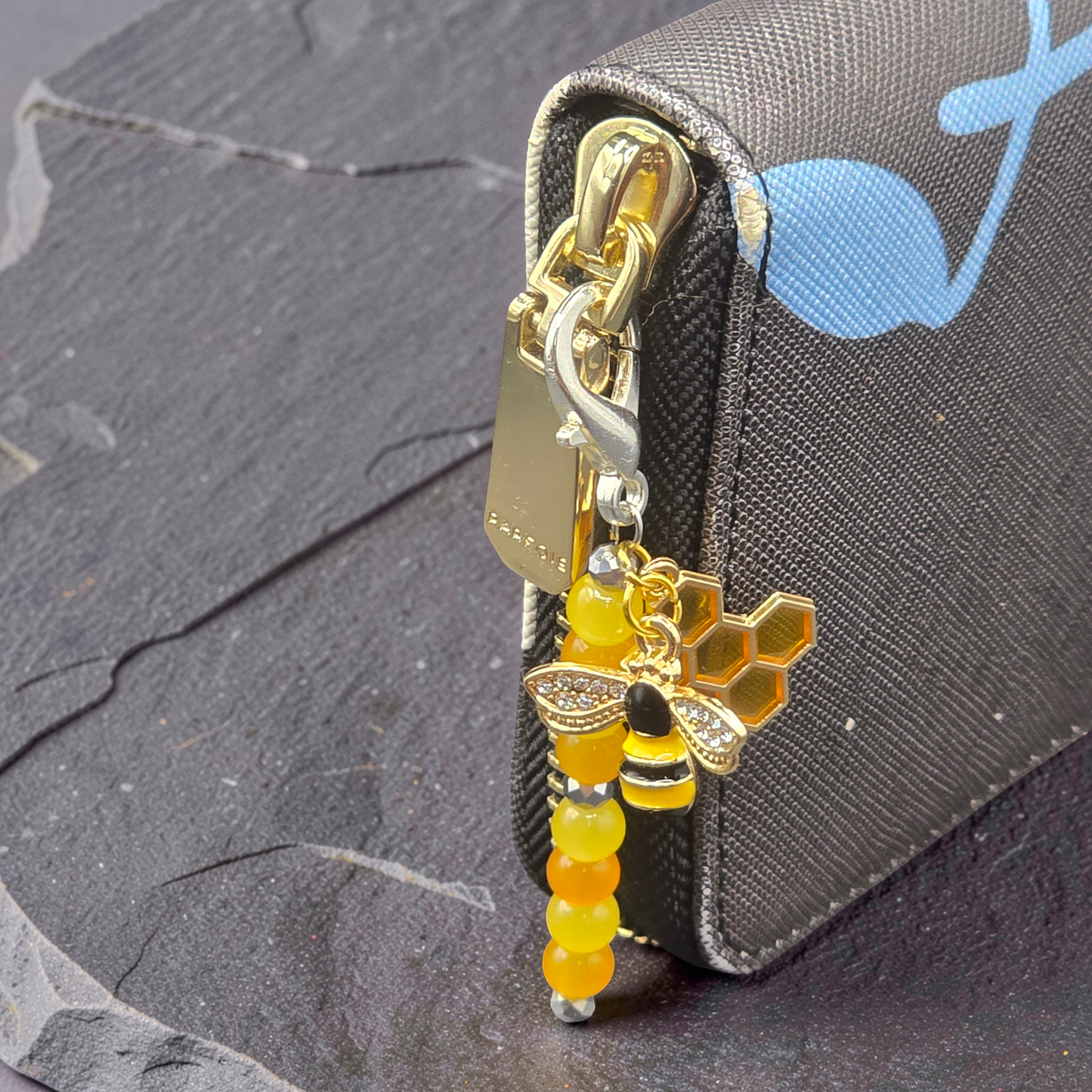 Bee themed zip charm attached to a gold zip on a purse
