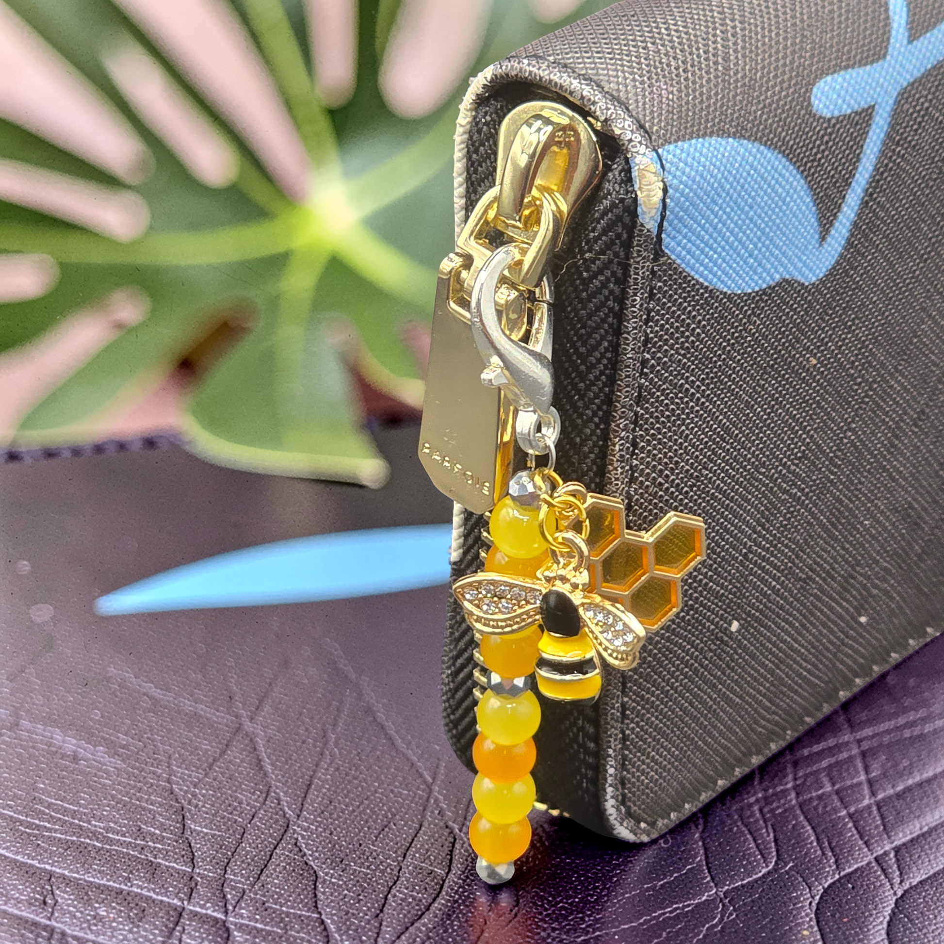 Gold and silver zipper charm with bee and honeycomb design attached to a purse.