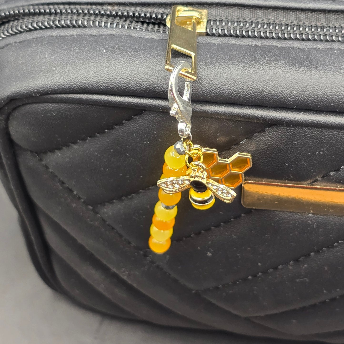 top down shot of a handmade zip charm featuring a bee and honeycomb design and beaded bar