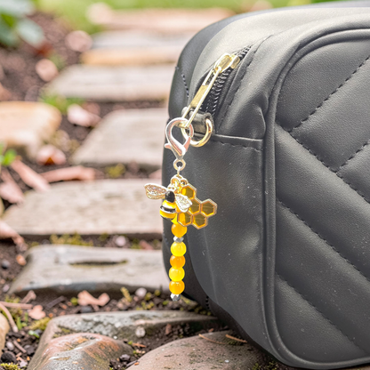 Bee themed bag charm with bee and honeycomb design attached to a black bag outdoors.