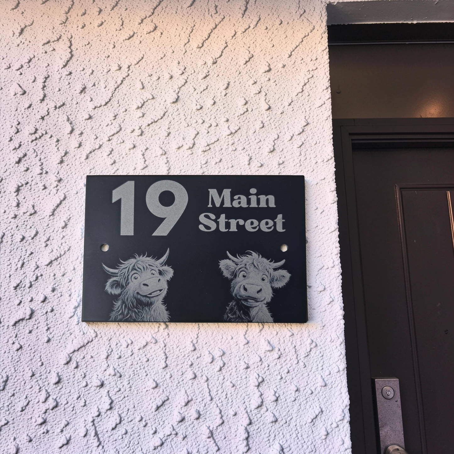 cute Highland cow House number sign with '19 Main Street' on a textured wall next to a door.
