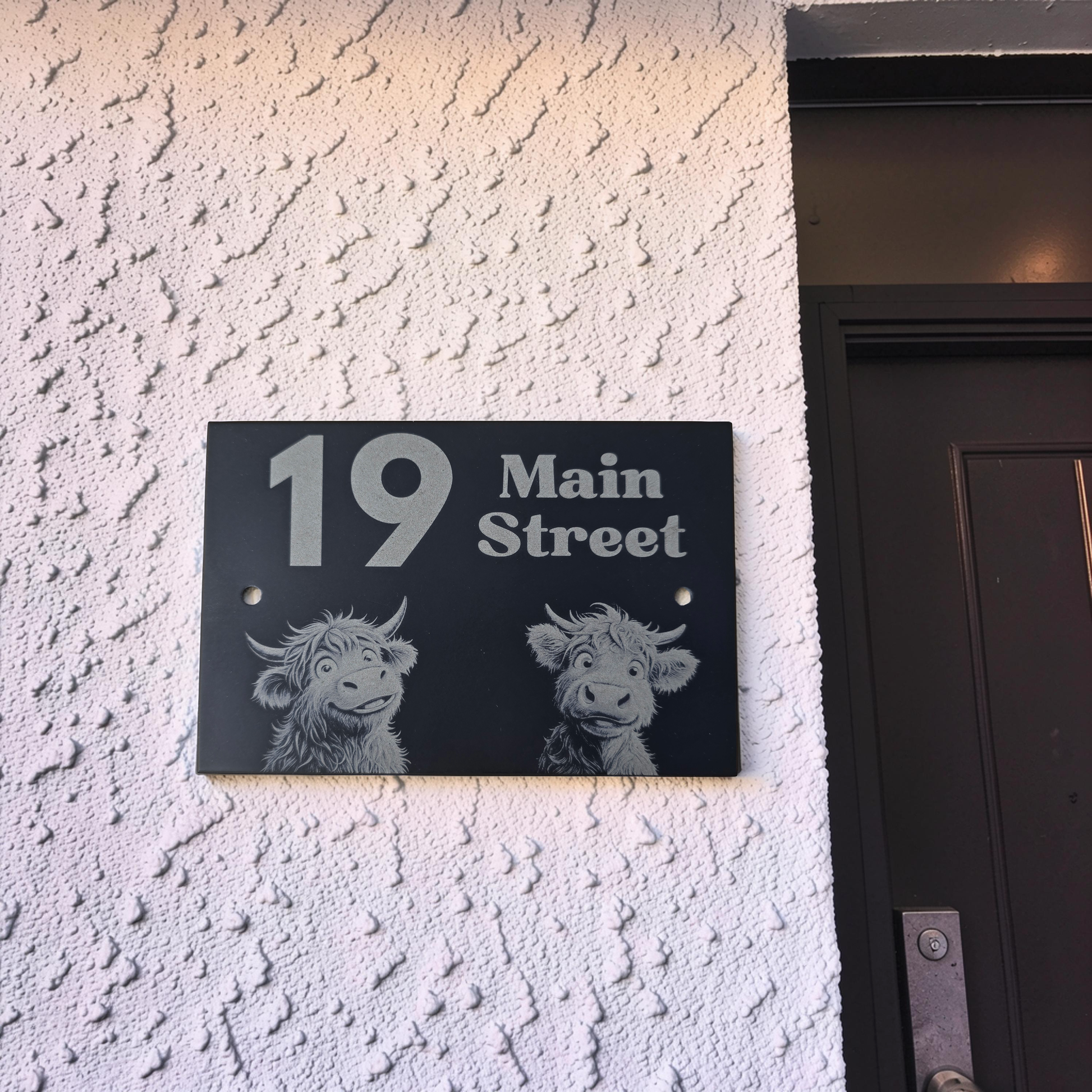 cute Highland cow House number sign with '19 Main Street' on a textured wall next to a door.