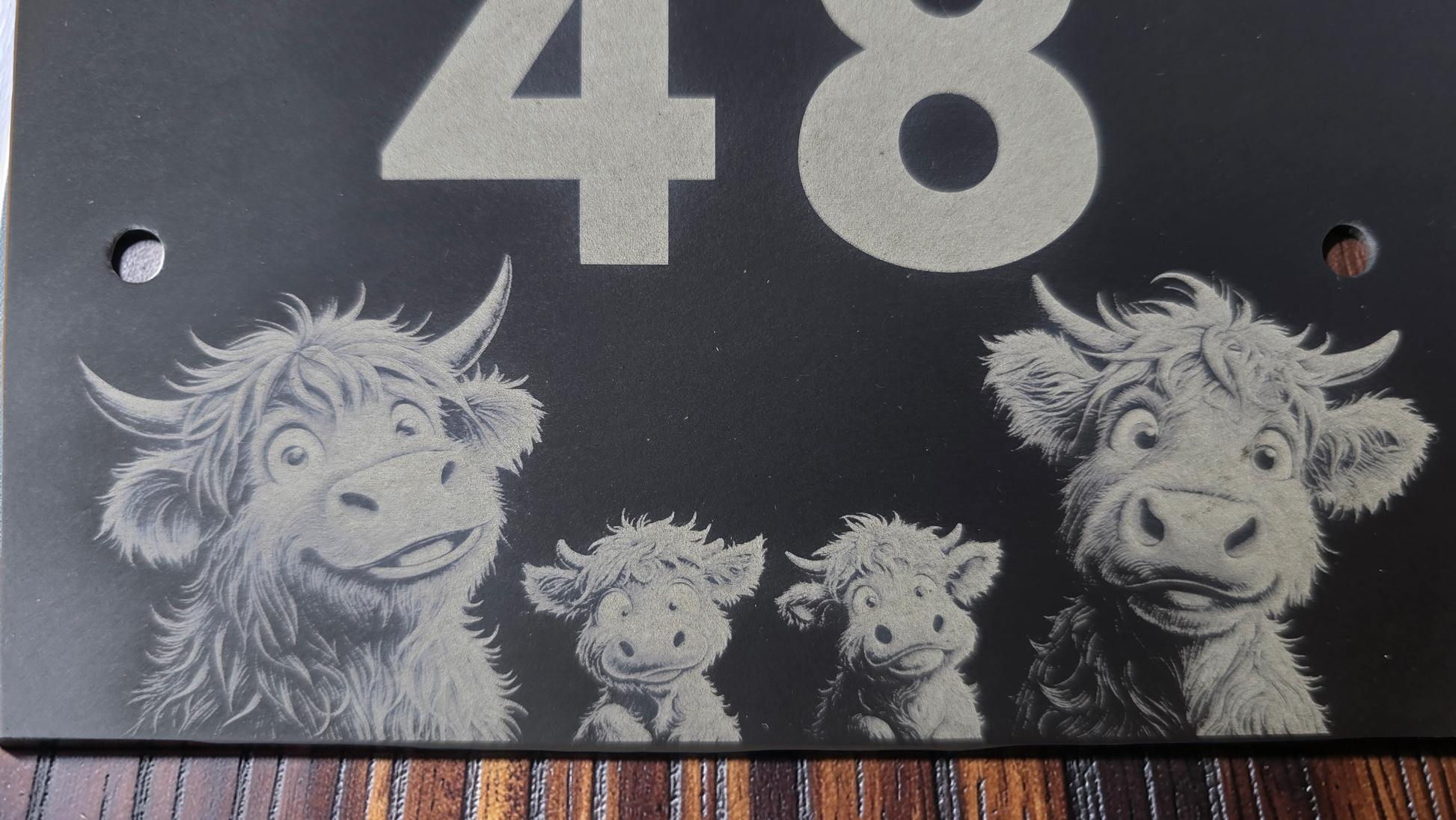 Decorative slate house plaque with four cartoon-style highland cows and the number 48 on a dark background.