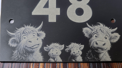 Decorative slate house plaque with four cartoon-style highland cows and the number 48 on a dark background.