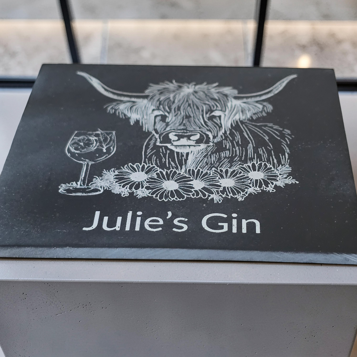 close up low angle shot of a personalised slate coaster with highland cow engraving and custom name text.