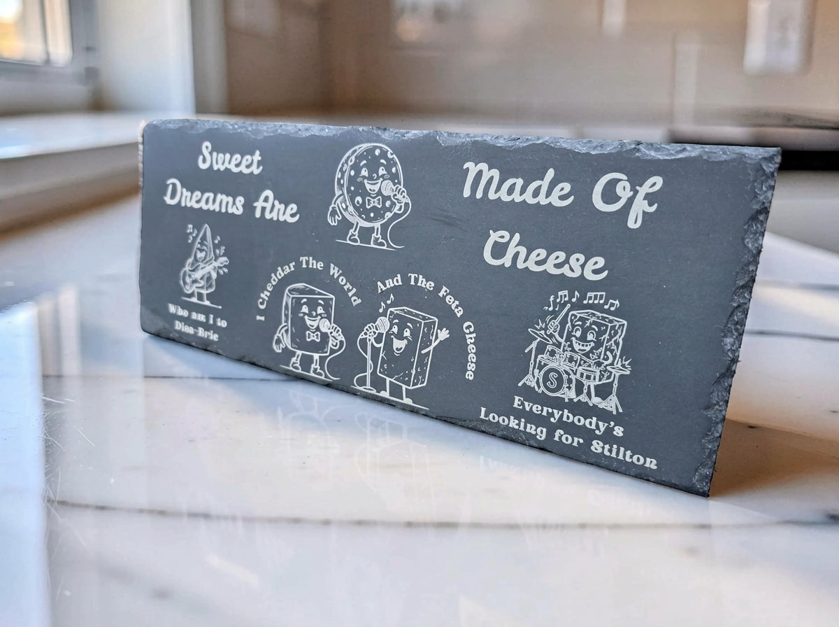 Dark rectangular slate board engraved with cartoon cheese characters and Sweet Dreams Are Made of Cheese pun lyrics.