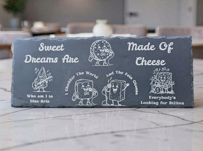 Dark slate cheese board engraved with cartoon cheese characters and the pun Sweet Dreams Are Made of Cheese.