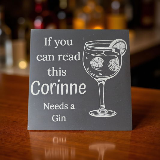 Personalized slate coaster with a glass of gin and text on a wooden surface.