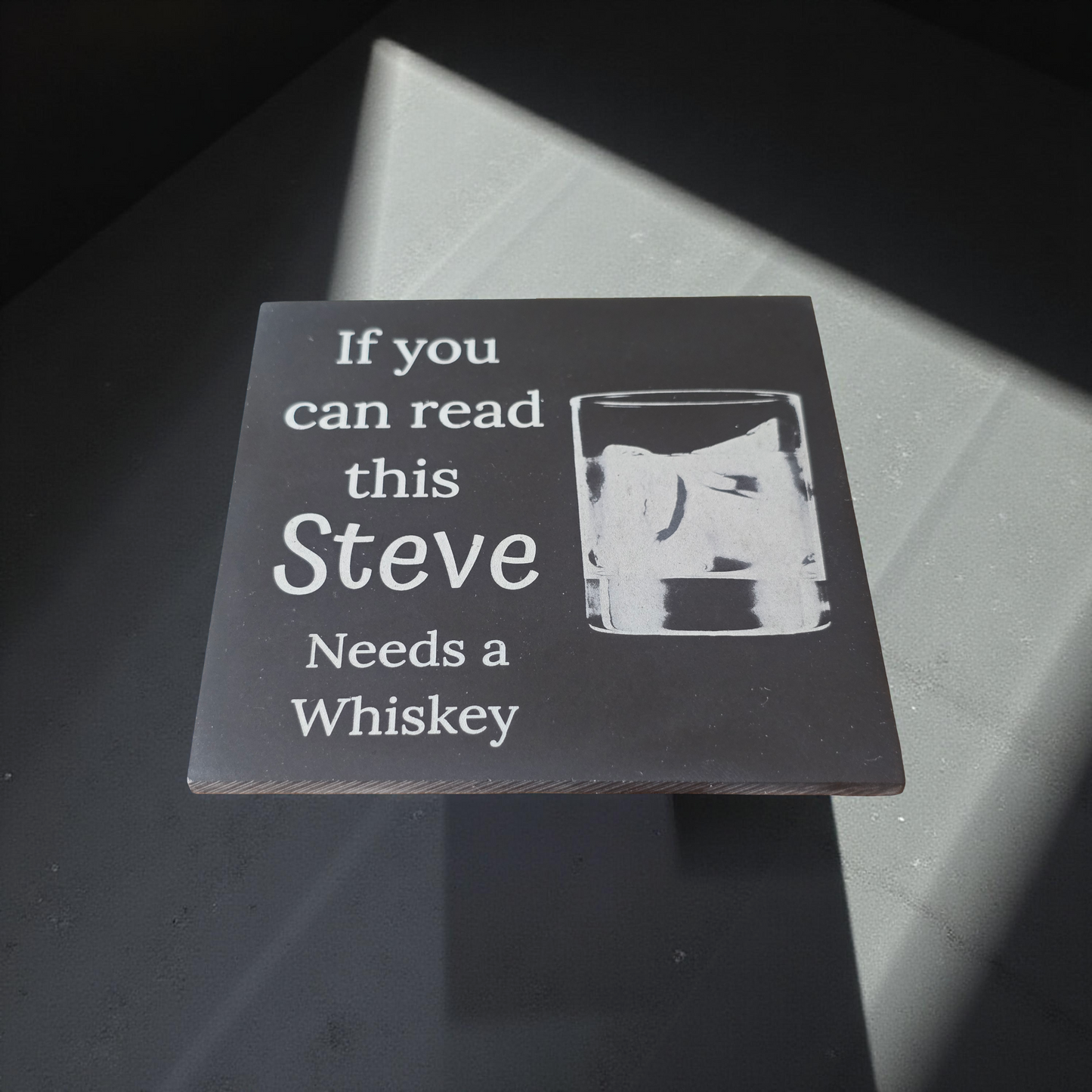Personalised coaster with text and whiskey glass illustration on a dark surface