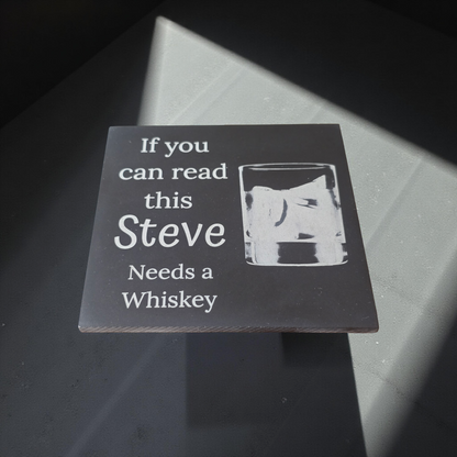 Personalised coaster with text and whiskey glass illustration on a dark surface