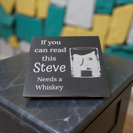 Slate Coaster with text 'If you can read this Steve Needs a Whiskey' on a marble surface.