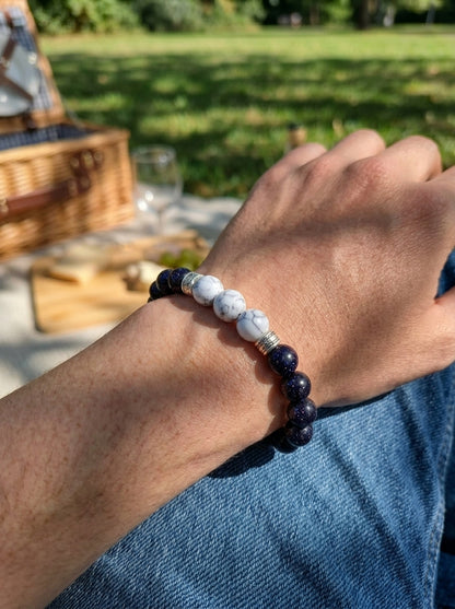 A beaded bracelet worn on a person's wrist, featuring dark navy blue and white marbled beads, photographed outdoors in a sunny park setting.