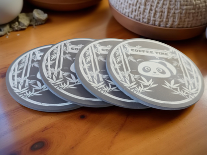 Set of four grey round slate coasters with tired panda designs on a wooden surface