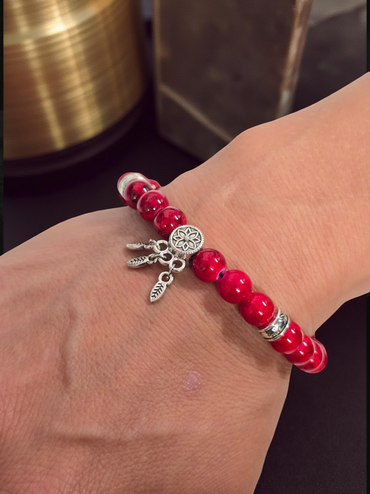 Red beaded bracelet with silver dreamcatcher charms on a wrist against a dark background