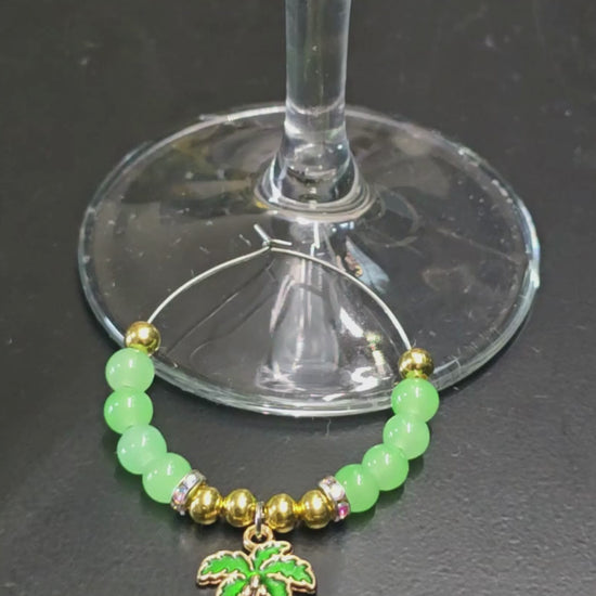 Green and gold tropical glass charm with palm tree, being placed onto a wine glass 