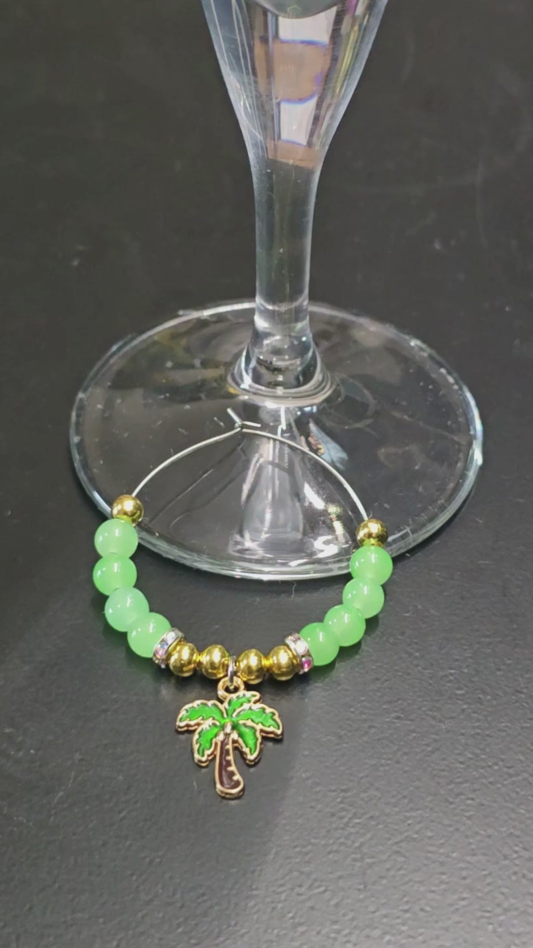 Green and gold tropical glass charm with palm tree, being placed onto a wine glass 