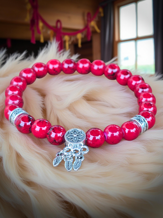 Red beaded bracelet with a silver dreamcatcher charm on a fluffy white rug